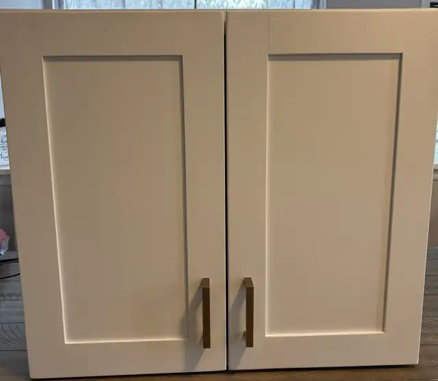 Close-up of white shaker cabinet doors with a smooth sprayed finish and brass bar pulls