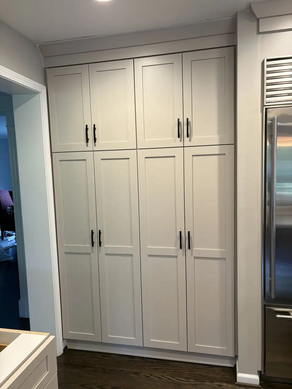 White shaker pantry cabinets with black pulls beside a stainless refrigerator, kitchen remodeling in Westland, MI by KGF Home Improvement